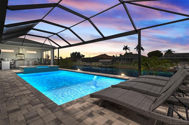 pool at dusk with glass enclosure, area for grilling, an in ground hot tub, and a patio