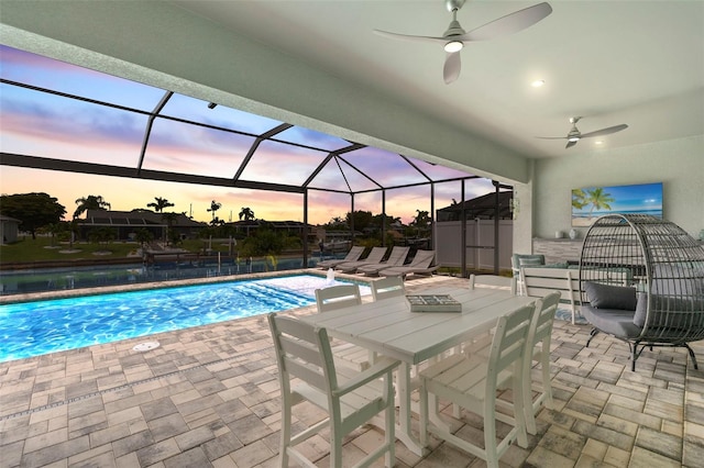 pool at dusk featuring a patio, ceiling fan, and a lanai