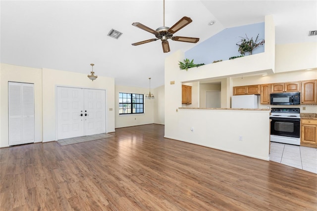 unfurnished living room with hardwood / wood-style flooring, ceiling fan with notable chandelier, and high vaulted ceiling