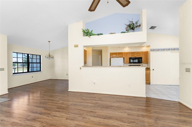 unfurnished living room with ceiling fan with notable chandelier, high vaulted ceiling, and light hardwood / wood-style flooring