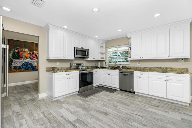 kitchen featuring white cabinetry, sink, light hardwood / wood-style flooring, dark stone counters, and appliances with stainless steel finishes