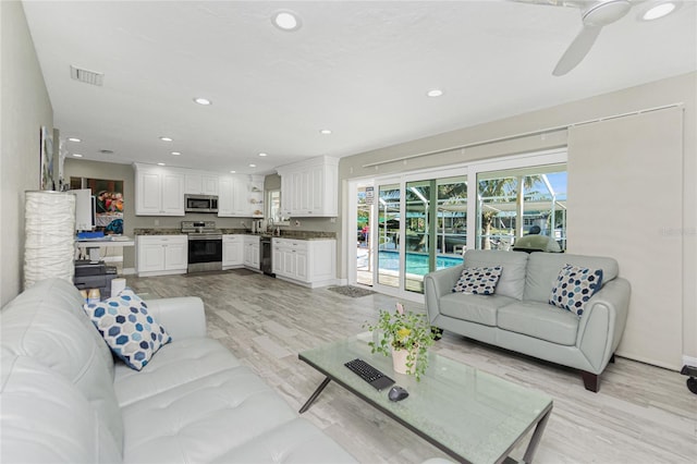 living room featuring sink, light wood-type flooring, plenty of natural light, and ceiling fan