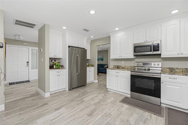 kitchen featuring white cabinets, appliances with stainless steel finishes, light wood-type flooring, and dark stone counters