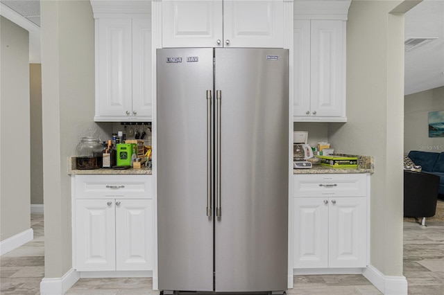 kitchen featuring light stone countertops, high end refrigerator, and white cabinets