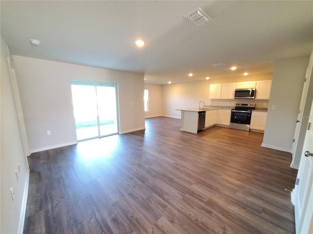 kitchen with a peninsula, dark wood-type flooring, white cabinets, appliances with stainless steel finishes, and open floor plan