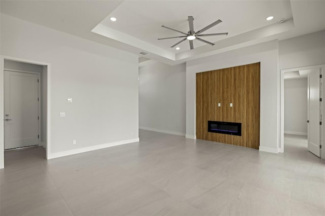 unfurnished living room featuring a large fireplace, a raised ceiling, and ceiling fan