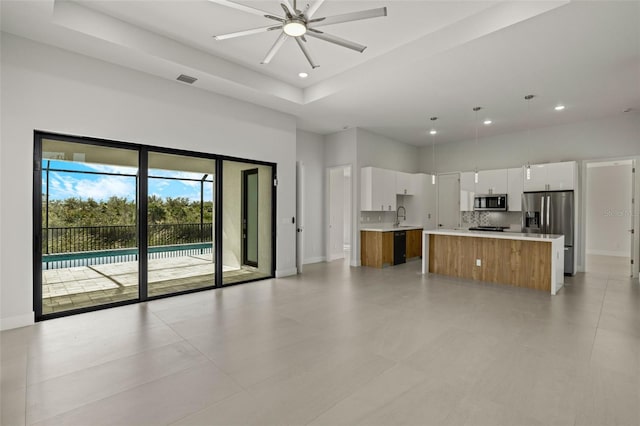 kitchen with appliances with stainless steel finishes, ceiling fan, a large island with sink, pendant lighting, and white cabinets