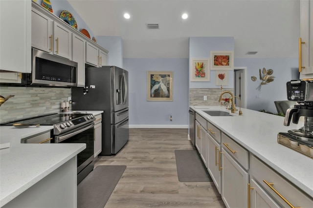 kitchen featuring decorative backsplash, appliances with stainless steel finishes, gray cabinetry, sink, and light hardwood / wood-style flooring