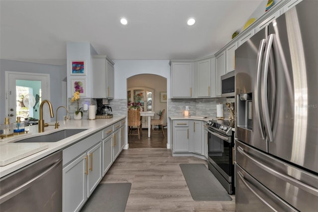 kitchen with decorative backsplash, sink, stainless steel appliances, and light hardwood / wood-style flooring