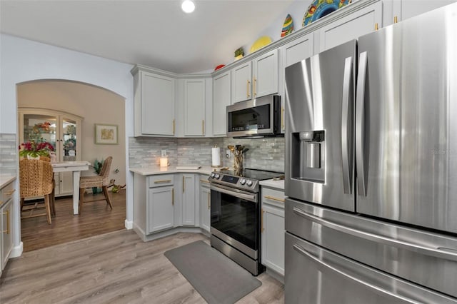 kitchen featuring light wood-type flooring, stainless steel appliances, and backsplash