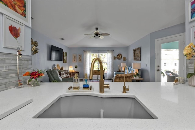 kitchen featuring light stone countertops, backsplash, ceiling fan, and sink