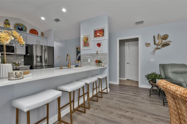 kitchen featuring a breakfast bar area, kitchen peninsula, stainless steel appliances, and vaulted ceiling