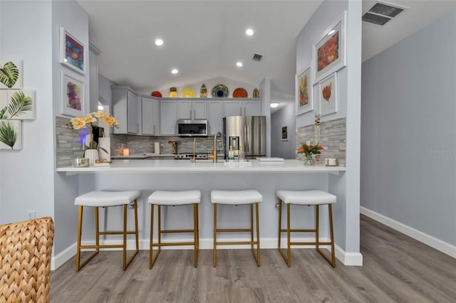 kitchen with stainless steel appliances, light hardwood / wood-style flooring, backsplash, kitchen peninsula, and vaulted ceiling