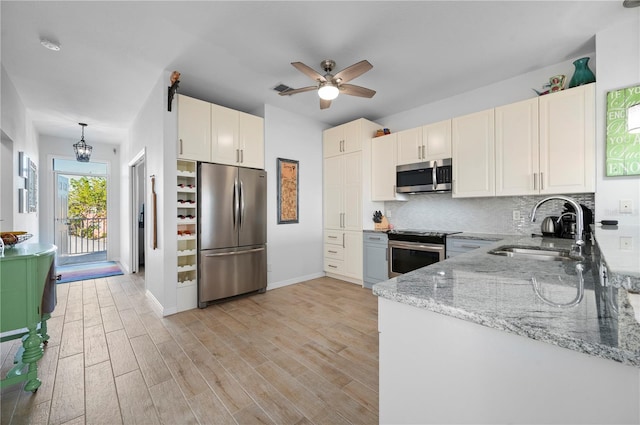 kitchen featuring pendant lighting, backsplash, sink, light stone countertops, and stainless steel appliances