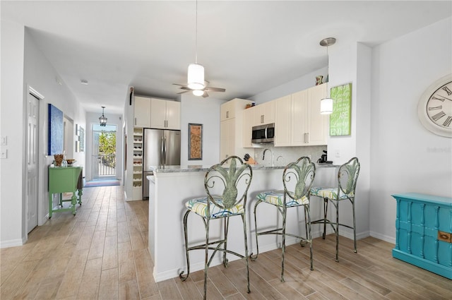 kitchen featuring kitchen peninsula, white cabinets, stainless steel appliances, and decorative light fixtures