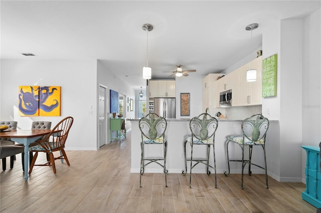 kitchen featuring kitchen peninsula, a kitchen bar, stainless steel appliances, ceiling fan, and white cabinets