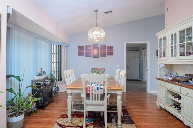 dining room featuring a chandelier, vaulted ceiling, and light wood-type flooring