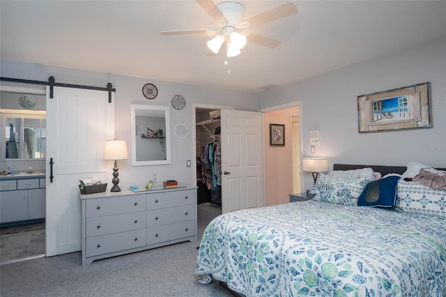 carpeted bedroom featuring a walk in closet, ceiling fan, a barn door, connected bathroom, and a closet