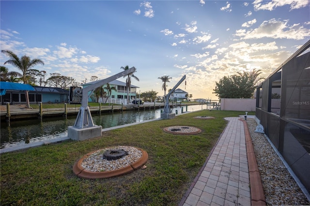 yard at dusk with a water view, a dock, glass enclosure, and a fire pit