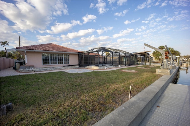 rear view of property with a water view, glass enclosure, and a lawn