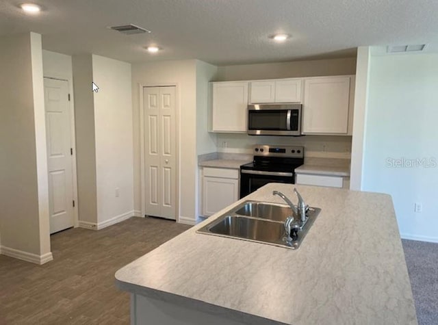 kitchen featuring white cabinetry, sink, stainless steel appliances, dark hardwood / wood-style flooring, and a center island with sink