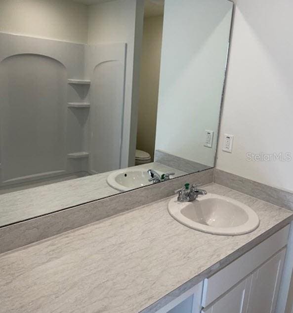 bathroom with walk in shower, vanity, and toilet