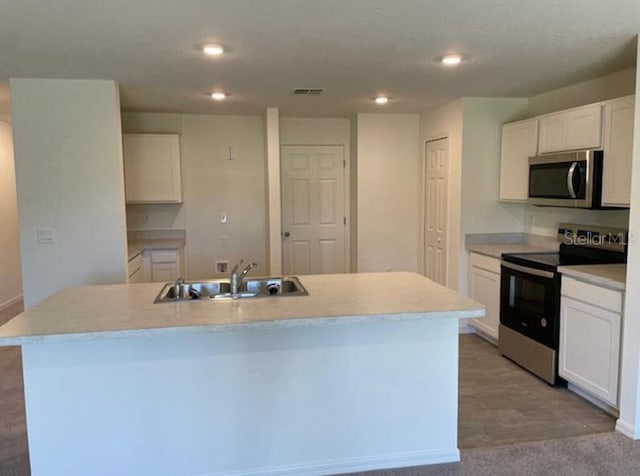 kitchen with light carpet, stainless steel appliances, a kitchen island with sink, sink, and white cabinetry