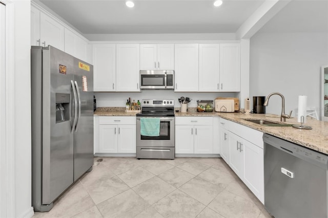 kitchen featuring white cabinets, sink, appliances with stainless steel finishes, light stone counters, and kitchen peninsula