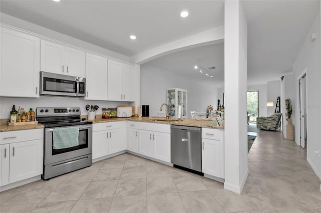 kitchen featuring white cabinets, sink, appliances with stainless steel finishes, light stone counters, and kitchen peninsula