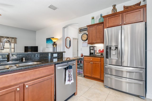 kitchen with sink, dark stone countertops, light tile patterned floors, stainless steel appliances, and beverage cooler