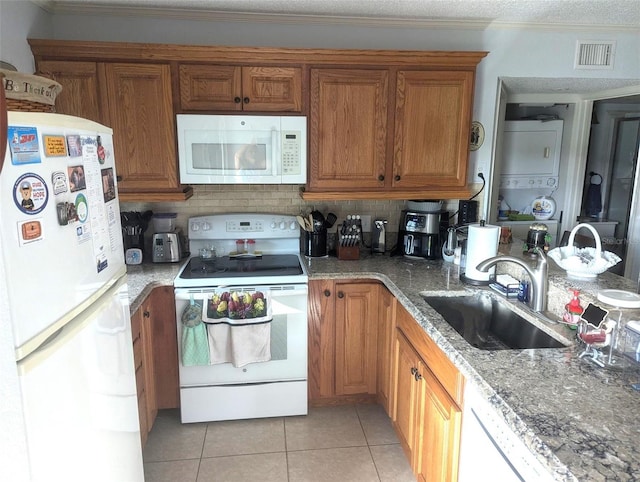 kitchen featuring sink, backsplash, dark stone counters, white appliances, and light tile patterned floors