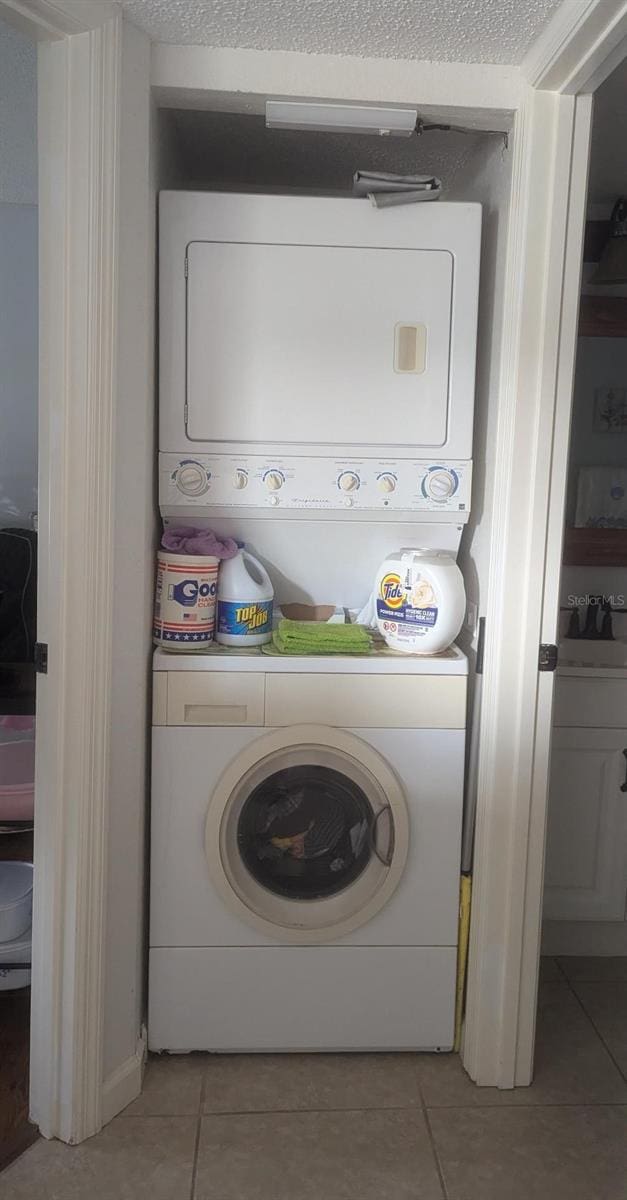 laundry room featuring a textured ceiling, stacked washer and dryer, and light tile patterned flooring