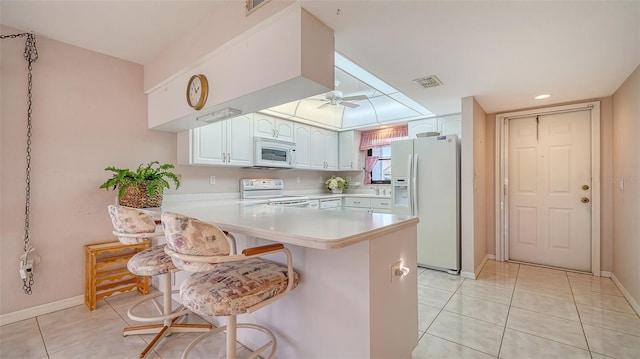 kitchen with ceiling fan, kitchen peninsula, white appliances, a breakfast bar area, and white cabinets