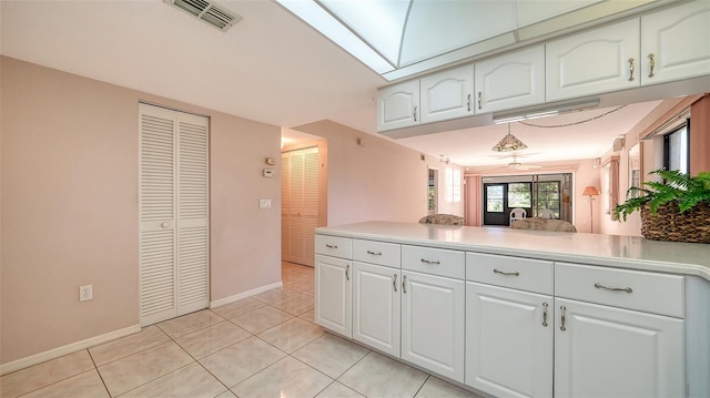 kitchen with white cabinetry, kitchen peninsula, light tile patterned floors, and a skylight