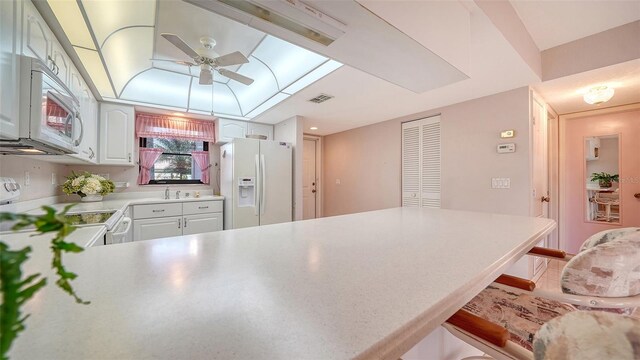 kitchen featuring ceiling fan, a breakfast bar area, a peninsula, white appliances, and light countertops