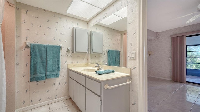 bathroom with a skylight, wallpapered walls, vanity, baseboards, and tile patterned floors