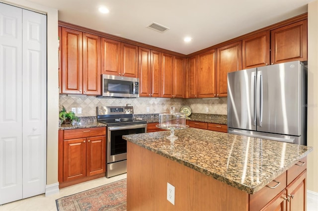 kitchen with backsplash, dark stone countertops, a kitchen island, and appliances with stainless steel finishes