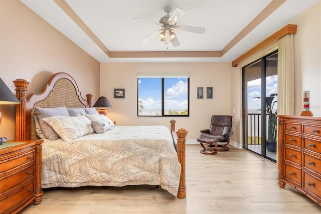 bedroom featuring access to exterior, light hardwood / wood-style floors, ceiling fan, and a tray ceiling