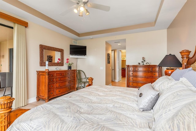 bedroom with a tray ceiling, ceiling fan, and light wood-type flooring