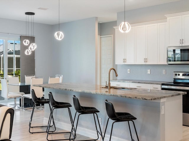 kitchen featuring decorative light fixtures, white cabinetry, light wood-type flooring, and appliances with stainless steel finishes