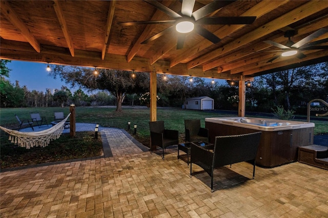 patio terrace at dusk featuring a yard, a hot tub, ceiling fan, and an outdoor structure