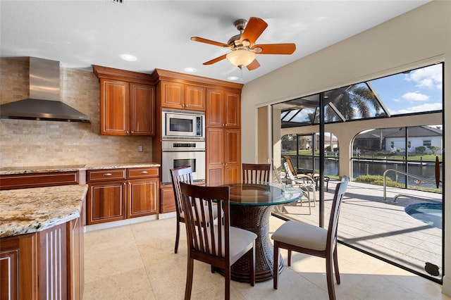 kitchen featuring backsplash, a water view, wall chimney exhaust hood, ceiling fan, and stainless steel appliances