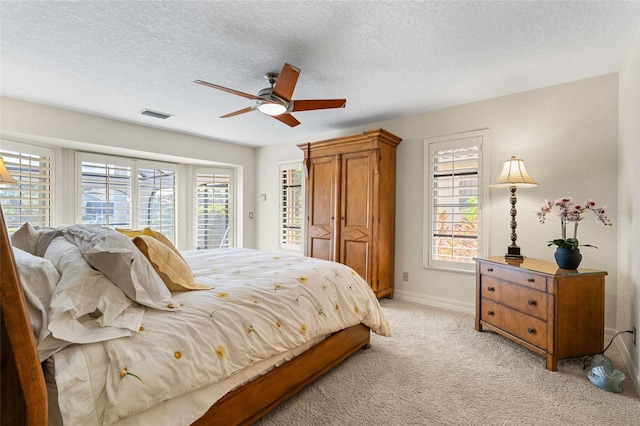 bedroom with ceiling fan, light colored carpet, and a textured ceiling