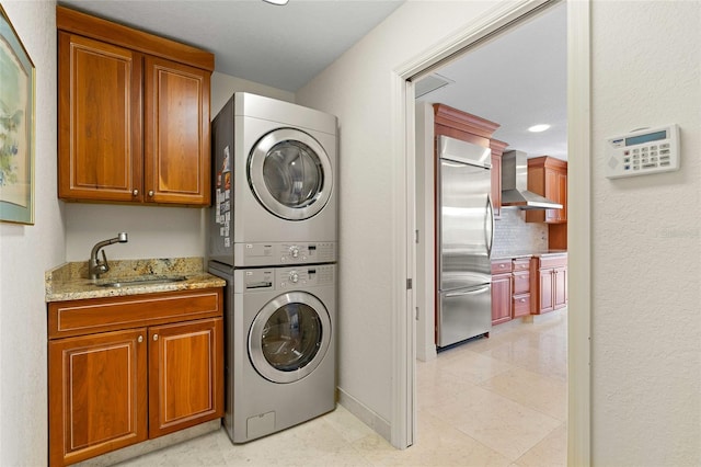 clothes washing area with cabinets, light tile patterned floors, stacked washer and clothes dryer, and sink