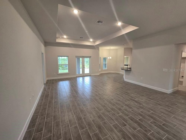 unfurnished living room with a tray ceiling, french doors, recessed lighting, wood tiled floor, and baseboards