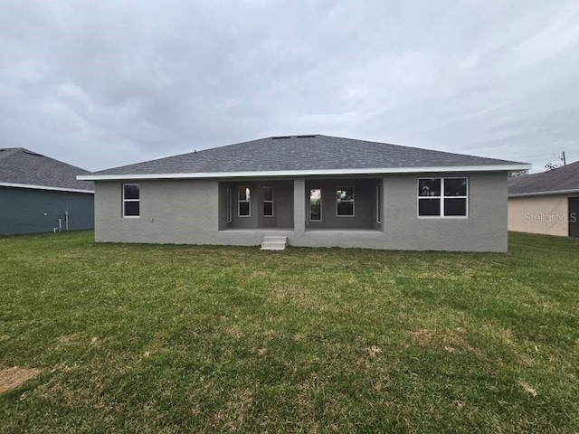 rear view of property with stucco siding, roof with shingles, and a yard