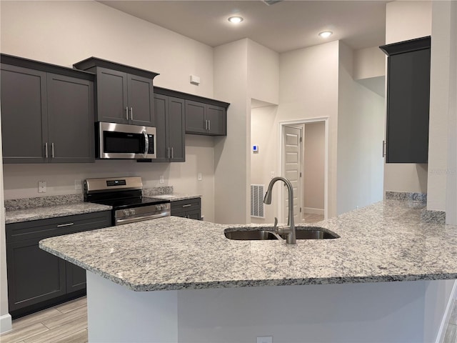 kitchen with stainless steel appliances, light stone countertops, sink, and kitchen peninsula