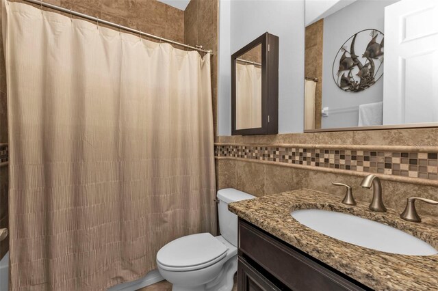 bathroom with curtained shower, vanity, tile walls, and toilet