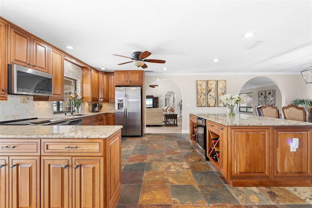 kitchen featuring light stone counters, stainless steel appliances, ceiling fan, crown molding, and sink