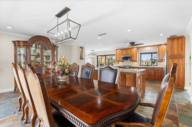 dining space with ceiling fan with notable chandelier, crown molding, and sink